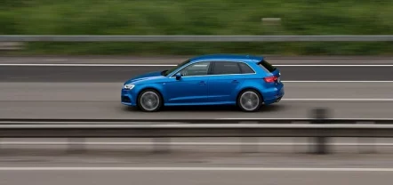 Schnell fahrendes Auto in der Seitenansicht auf einer Straße mit Leitplanke