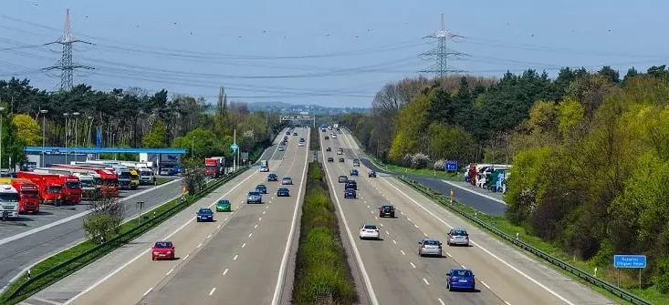 Blick von einer Brücke auf eine dreispurige Autobahn mit fließendem Verkehr in beiden Fahrtrichtungen