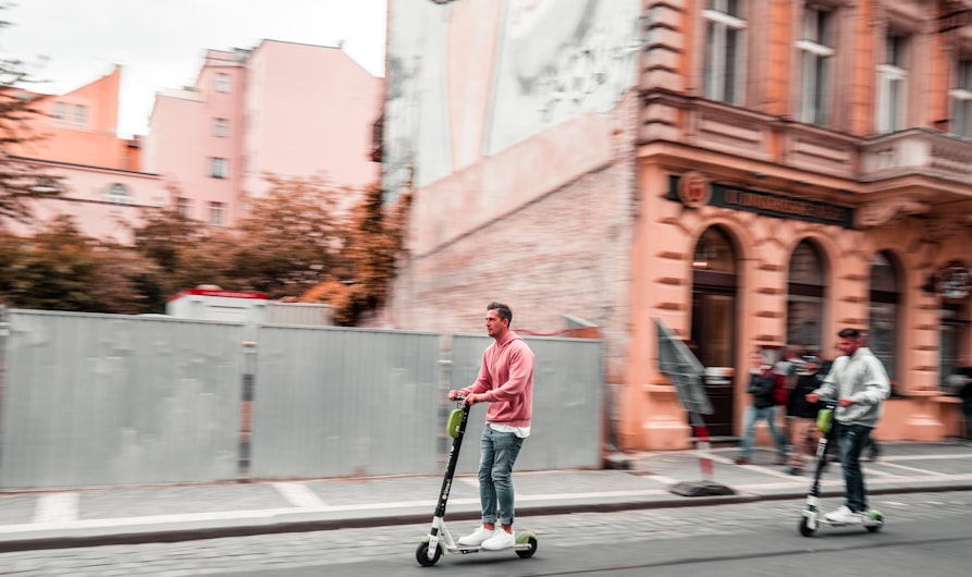 two men riding kick scooters during daytime